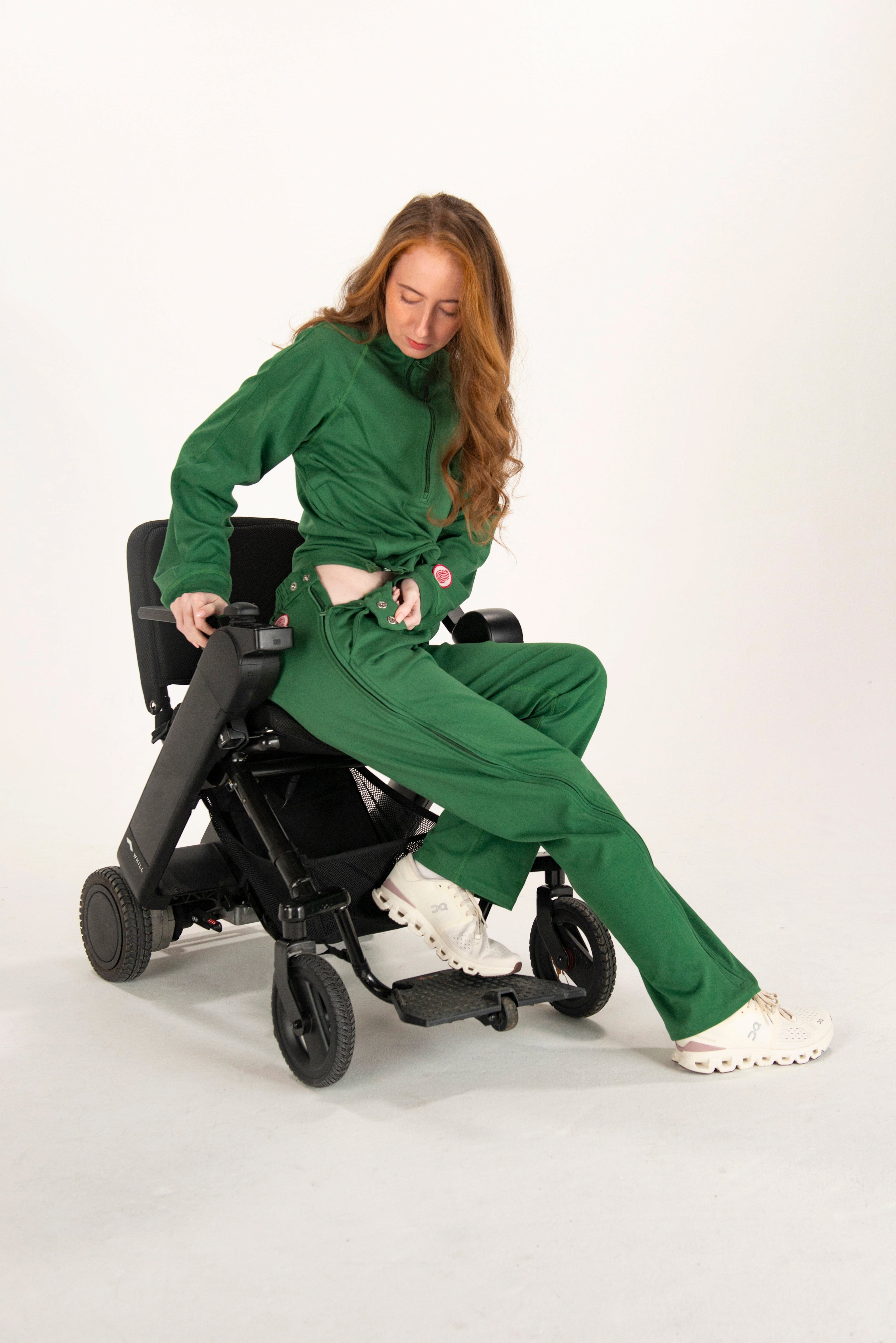 Person in a green outfit using a power wheelchair on a white background